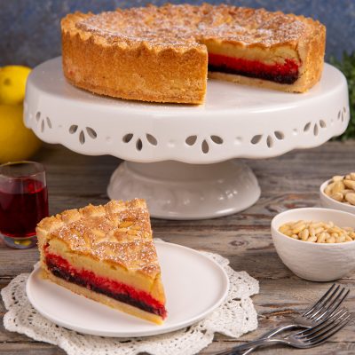 Torta delle zitelle con uno spicchio servito a parte, che rivela il ripieno di crema e confettura rossa
