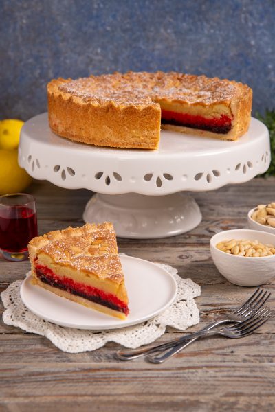 Torta delle zitelle con uno spicchio servito a parte, che rivela il ripieno di crema e confettura rossa