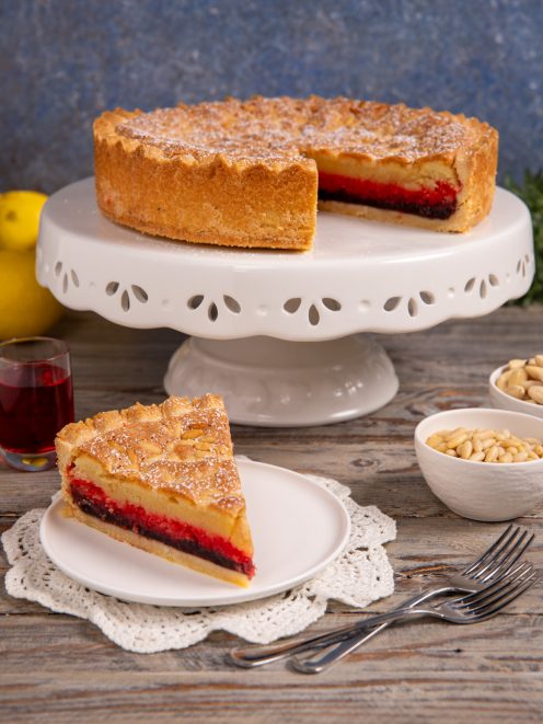 Torta delle zitelle con uno spicchio servito a parte, che rivela il ripieno di crema e confettura rossa