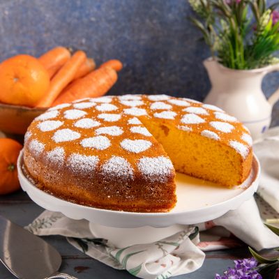 Torta di carote con zucchero a velo decorato a cuori, una fetta già tagliata rivela l'interno dorato