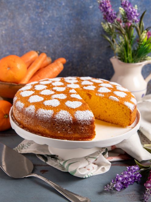 Torta di carote con zucchero a velo decorato a cuori, una fetta già tagliata rivela l'interno dorato