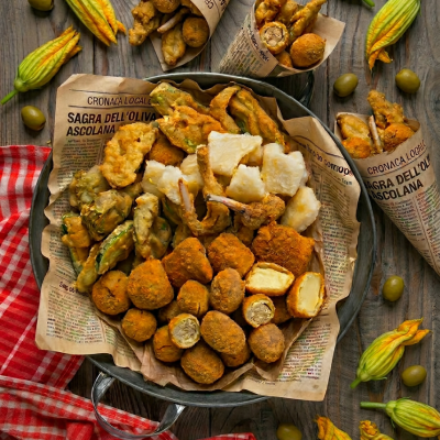 Cartoccio ascolana con olive fritte, fiori di zucca in pastella, baccalà e verdure miste serviti su carta di giornale
