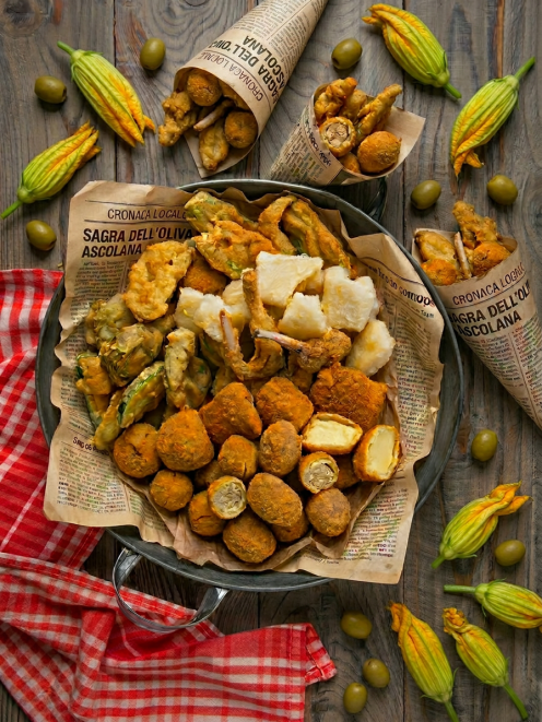 Cartoccio ascolana con olive fritte, fiori di zucca in pastella, baccalà e verdure miste serviti su carta di giornale