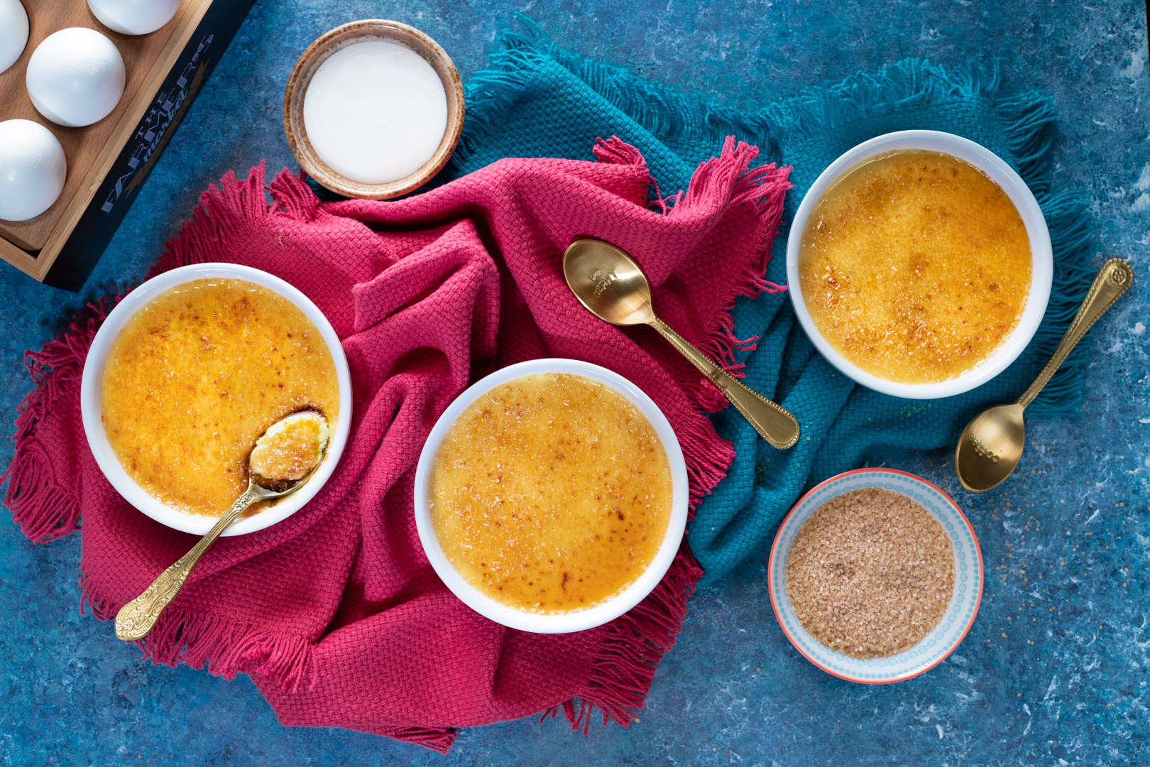 Tre crème brûlée con crosticina caramellata dorata, una già aperta con il cucchiaio