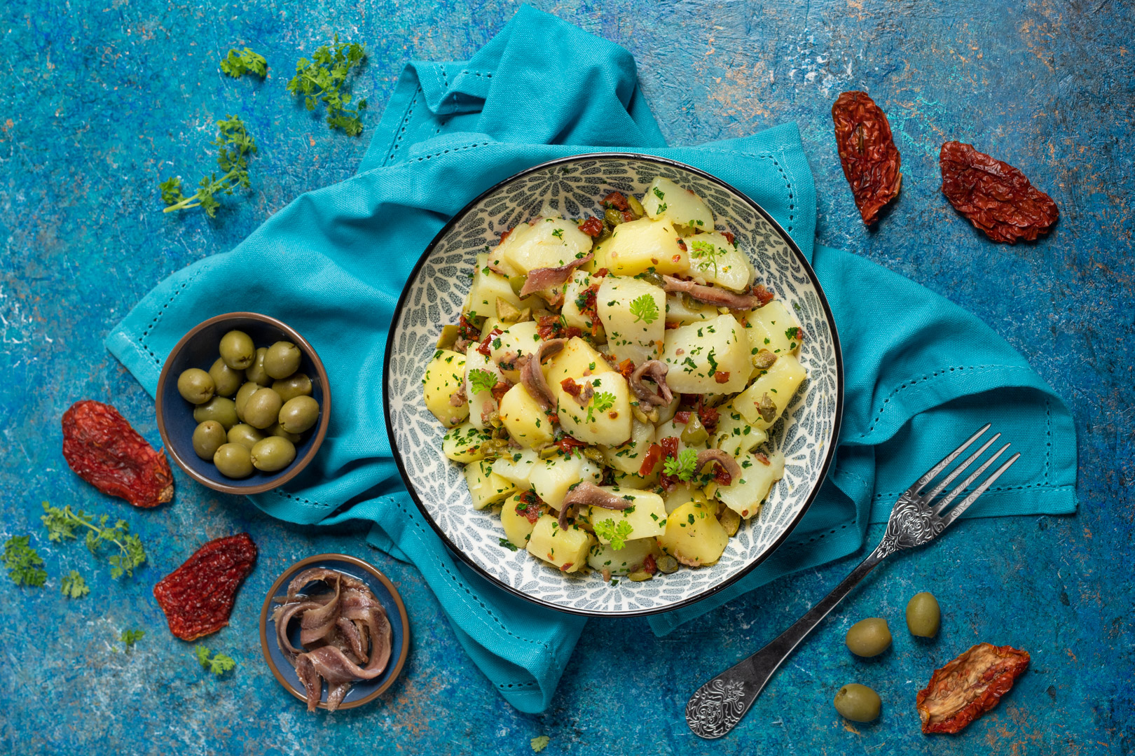 Insalata di patate condita con alici, olive verdi, pomodori secchi e prezzemolo tritato