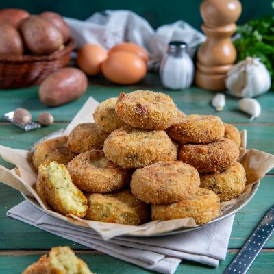Polpette di patate fritte impilate con crosticina dorata, una spezzata rivela il ripieno morbido