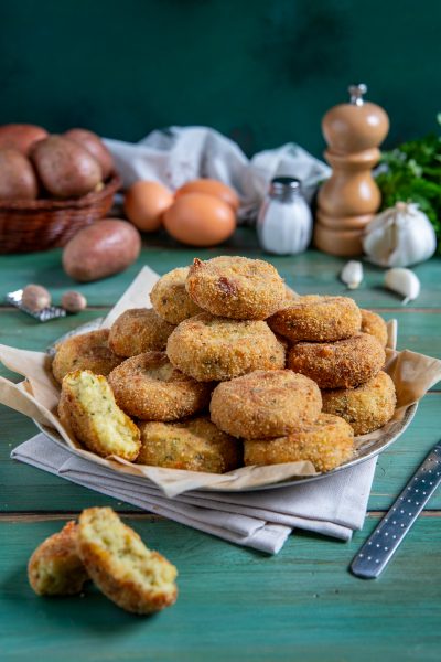 Polpette di patate fritte impilate con crosticina dorata, una spezzata rivela il ripieno morbido