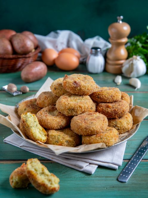 Polpette di patate fritte impilate con crosticina dorata, una spezzata rivela il ripieno morbido