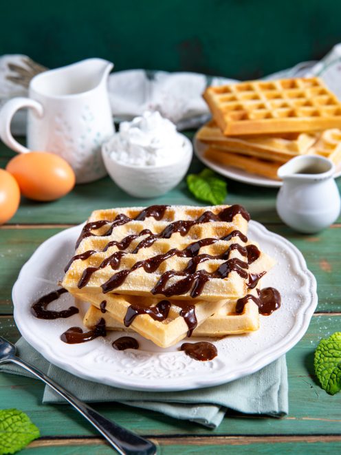 Waffle impilati con colata di salsa al cioccolato e zucchero a velo