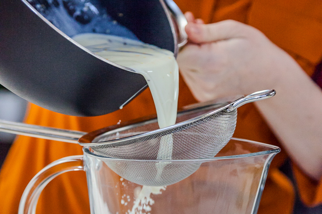 Crema alla vaniglia versata attraverso un colino a maglia fine in una caraffa