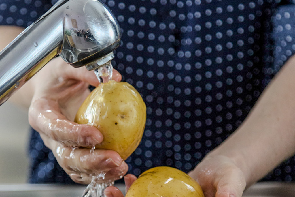 Mani che lavano due patate sotto l'acqua corrente del rubinetto