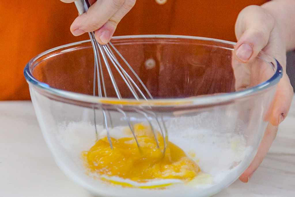 Tuorli d'uovo e zucchero mescolati con una frusta in una ciotola di vetro