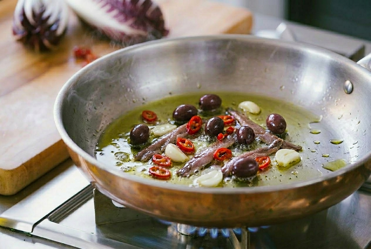 Acciughe, olive taggiasche, aglio e peperoncino a rondelle che sfrigolano nell'olio
