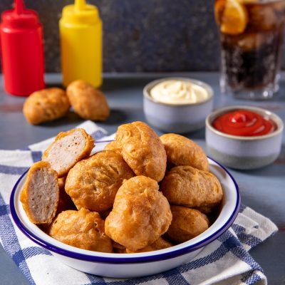 Nuggets di pollo fritti dorati in ciotola, uno spezzato mostra l'interno morbido