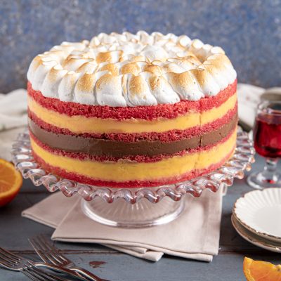 Torta zuppa inglese a strati con pan di Spagna rosso, crema gialla, crema al cioccolato e meringa tostata