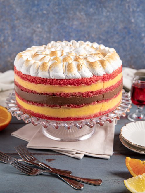 Torta zuppa inglese a strati con pan di Spagna rosso, crema gialla, crema al cioccolato e meringa tostata