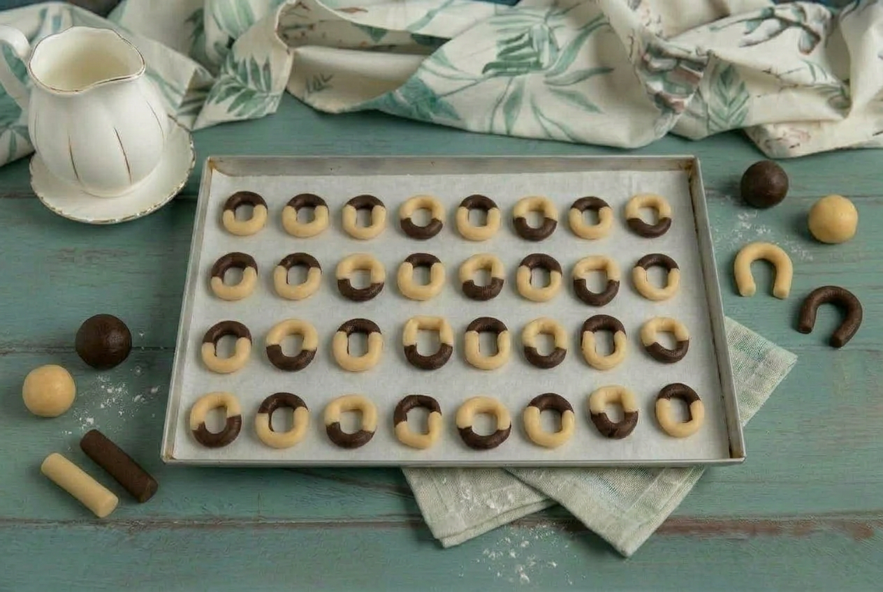 Biscotti bicolore a ferro di cavallo disposti in fila sulla teglia con carta forno, pronti per la cottura