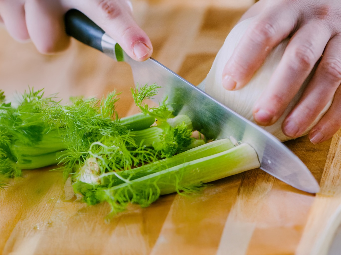 Mani che separano i gambi e le barbette dal finocchio con un coltello da chef