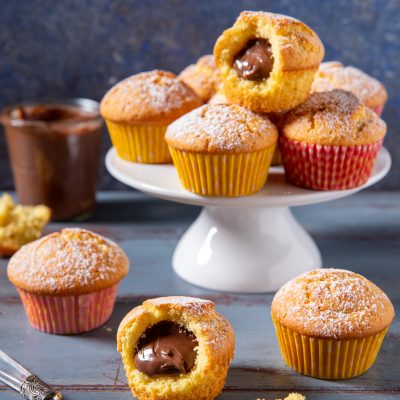 Muffin con cuore di Nutella spolverati di zucchero a velo, uno aperto a mostrare il ripieno morbido