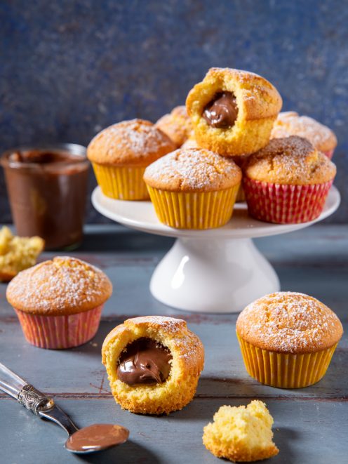 Muffin con cuore di Nutella spolverati di zucchero a velo, uno aperto a mostrare il ripieno morbido