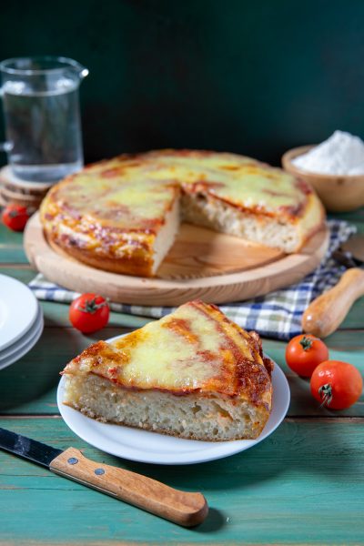 Pizza liquida con mozzarella filante e salsa di pomodoro, una fetta in primo piano che mostra l'impasto soffice e alveolato