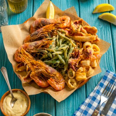 Fritto misto di pesce con gamberi, anelli di calamaro e verdure in pastella, servito su carta da pane con spicchio di limone