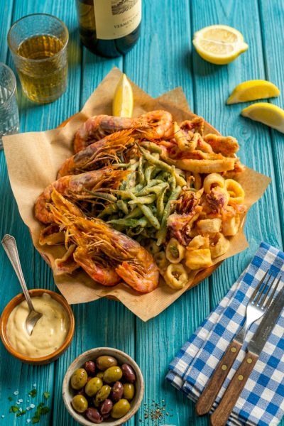 Fritto misto di pesce con gamberi, anelli di calamaro e verdure in pastella, servito su carta da pane con spicchio di limone