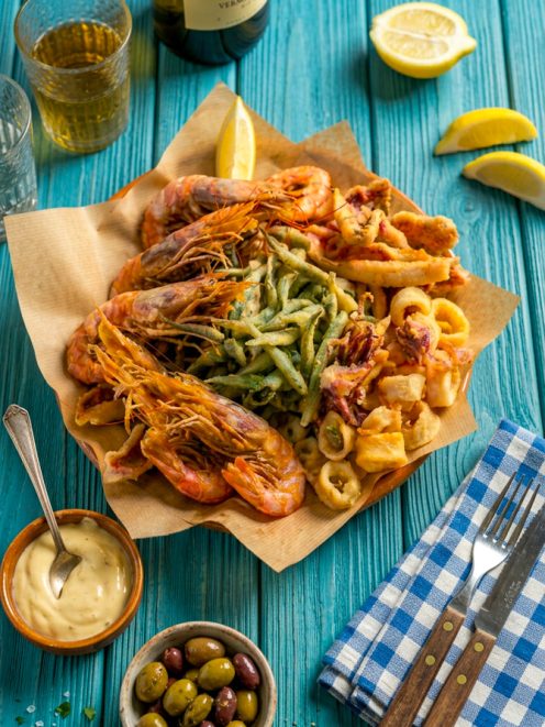 Fritto misto di pesce con gamberi, anelli di calamaro e verdure in pastella, servito su carta da pane con spicchio di limone