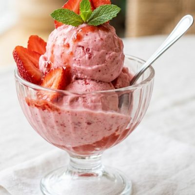 Gelato alla fragola servito con fettine di fragola fresca e foglioline di menta