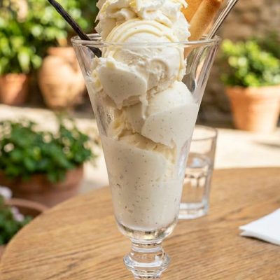 Gelato alla vaniglia in coppa con panna montata, scaglie di cioccolato bianco, biscotto e bacca di vaniglia