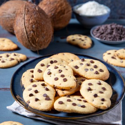 Gocciole al cocco impilate su un piatto con cocco fresco e gocce di cioccolato sullo sfondo