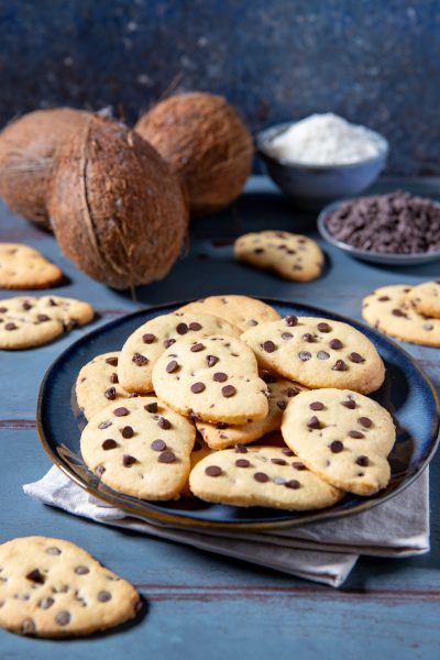 Gocciole al cocco impilate su un piatto con cocco fresco e gocce di cioccolato sullo sfondo