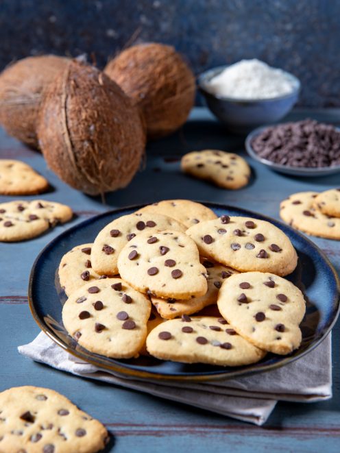 Gocciole al cocco impilate su un piatto con cocco fresco e gocce di cioccolato sullo sfondo