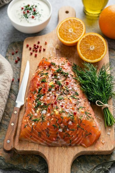 Salmone marinato con aneto fresco, sale grosso e pepe rosa, affiancato da arance tagliate a metà