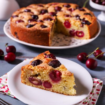 Torta di ciliegie e ricotta con una fetta servita in primo piano che mostra l'impasto soffice e le ciliegie intere