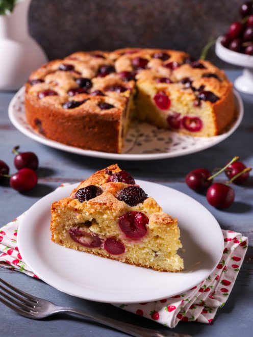 Torta di ciliegie e ricotta con una fetta servita in primo piano che mostra l'impasto soffice e le ciliegie intere