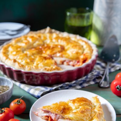 Torta salata di pasta sfoglia farcita con prosciutto, mozzarella e pomodoro, servita a fette