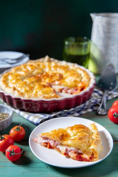 Torta salata di pasta sfoglia farcita con prosciutto, mozzarella e pomodoro, servita a fette