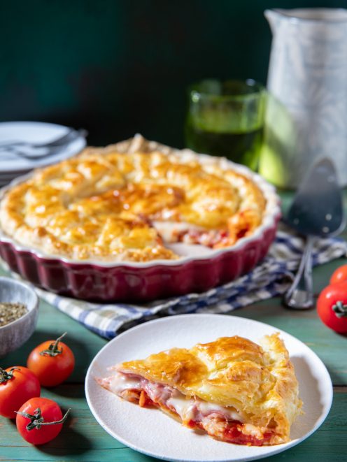 Torta salata di pasta sfoglia farcita con prosciutto, mozzarella e pomodoro, servita a fette