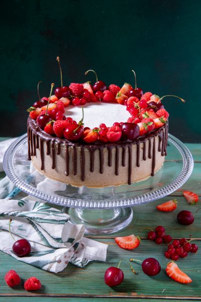 Drip cheesecake ai frutti rossi e ciliegie con colata di cioccolato e corona di fragole, lamponi e ciliegie fresche