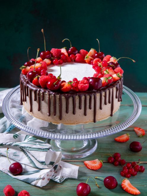 Drip cheesecake ai frutti rossi e ciliegie con colata di cioccolato e corona di fragole, lamponi e ciliegie fresche