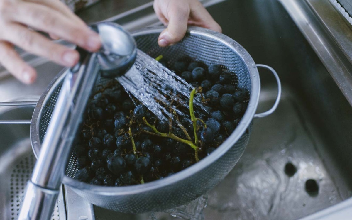 Acini di uva fragola sciacquati sotto l'acqua corrente in uno scolapasta