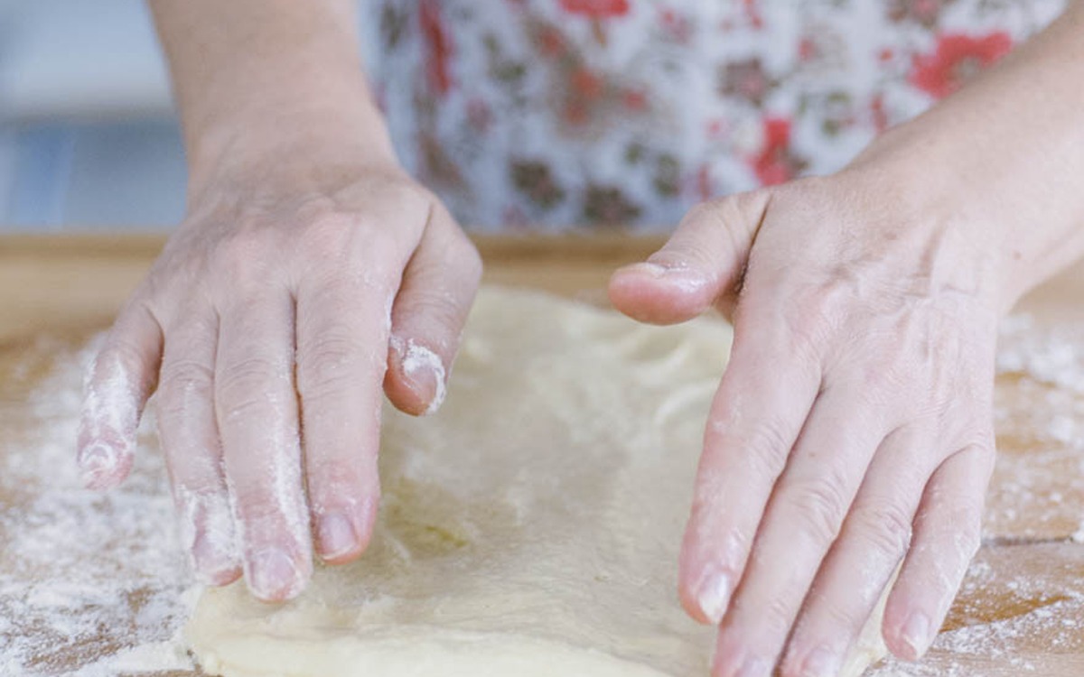 Mani che stendono l'impasto della ciaccia sul piano infarinato con i polpastrelli