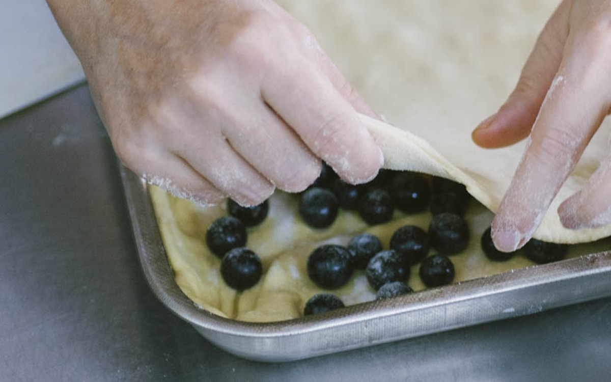 Mani che adagiano un foglio di pasta sull'uva fragola disposta nella teglia