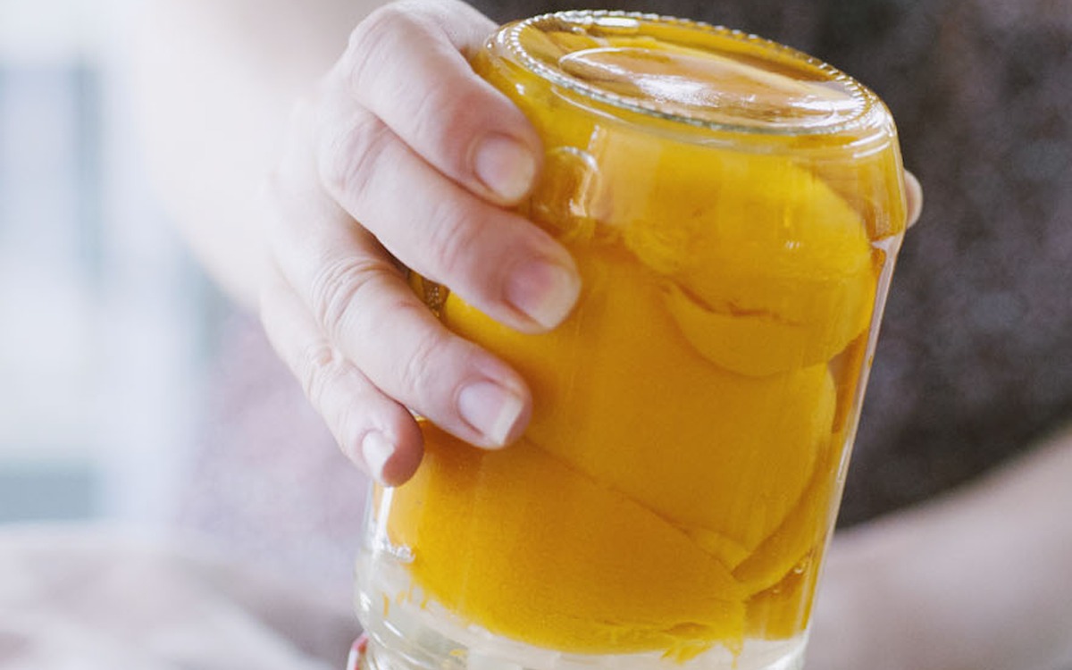 Mano che stringe un vasetto colmo di pesche sciroppate immerse nel liquido dorato