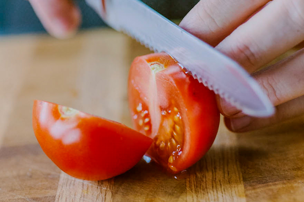 Un pomodoro tagliato a spicchi sul tagliere, con il coltello ancora in mano
