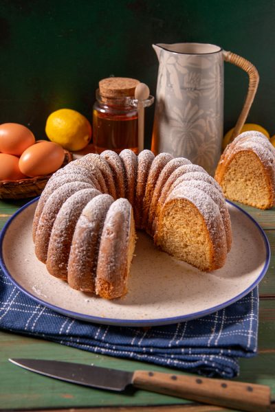 Ciambella al miele spolverata di zucchero a velo, con una fetta tagliata che mostra la mollica soffice