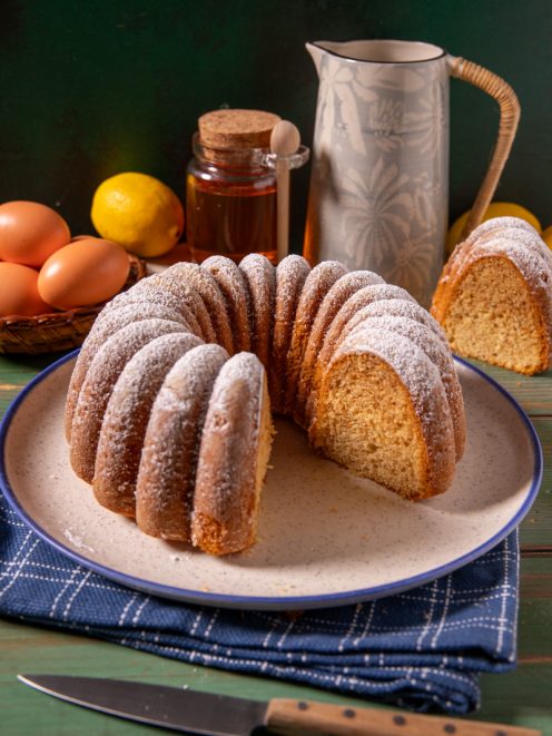Ciambella al miele spolverata di zucchero a velo, con una fetta tagliata che mostra la mollica soffice