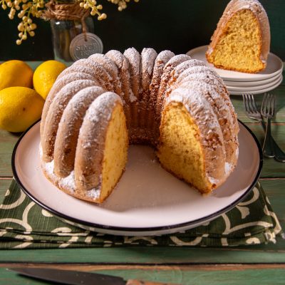 Ciambella soffice con una fetta tagliata, spolverata di zucchero a velo e mollica gialla ben alveolata
