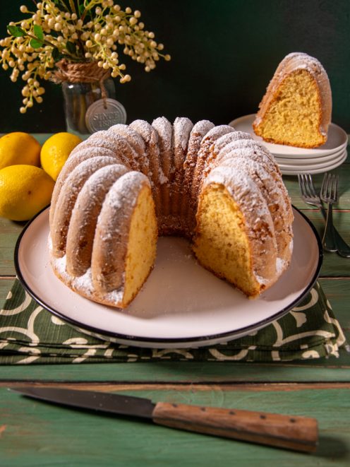 Ciambella soffice con una fetta tagliata, spolverata di zucchero a velo e mollica gialla ben alveolata